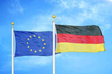 European Union and Germany two flags on flagpoles and blue cloudy sky