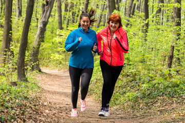 Mother and daughter wearing sportswear and running in forest.