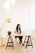 © Елизавета Старкова - Serious business working freelance woman with black hair in a business suit working on a laptop and phone at a wooden table against a white wall in a home office, business portrait