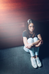 Battered woman sitting on the floor with her legs wrapped up in protection. Her face showing bruises and stitches under her eyes. , she appears small and with a frightened expression. 