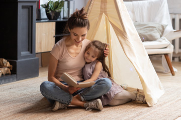 mom teaching smiling little daughter to read text.