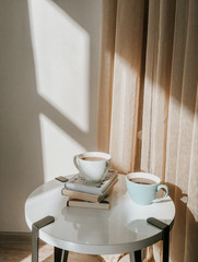 Warm cozy home. Couple cups of coffee with book on a white table . Sunshine appartment.