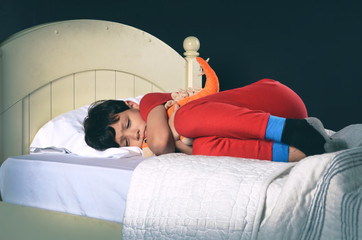 Little boy curled up on bed with stuffed animal