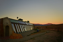 Front Side View Of Self Sustaining Eco-friendly Earth Ship Home At Sunset With Mountains In Background Of Landscape In Toas, New Mexico.