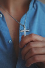 Vertical Closeup Shot Of A Male Holding A Silver Necklace With A Cross Pendant
