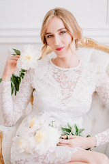 Beautiful bride in a white laced dress and wedding bouquet  is preparing for wedding ceremony in hotel room. Bride getting ready. Artwork