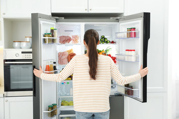 Canvas Print - Young woman opening refrigerator in kitchen, back view