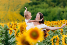 Happy Mother With The Daughter In The Field With Sunflowers. Mom And Baby Girl Having Fun Outdoors. Family Concept.