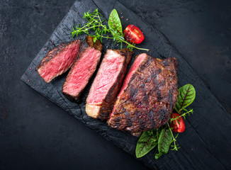 Barbecue dry aged wagyu entrecote beef steak with lettuce and tomatoes as top view on an old charred wooden board with copy space