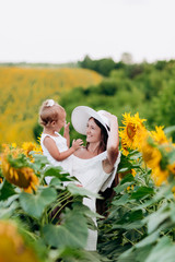 Wall Mural - Happy mother with the daughter in the field with sunflowers. mom and baby girl having fun outdoors. family concept.