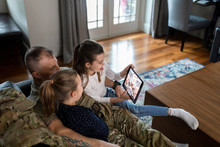 Soldier Father And Daughters Using Digital Tablet On Sofa