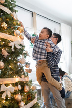 Boy Lifting Little Brother Helping With Christmas Tree Decorations