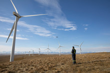 Male Wind Farm Technician Standing Among Wind Turbines In Remote Field