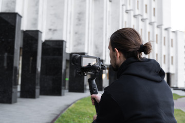 Wall Mural - Young Professional videographer holding professional camera on 3-axis gimbal stabilizer. Pro equipment helps to make high quality video without shaking. Cameraman wearing black hoodie making a videos.