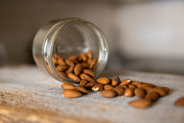 Almonds scattered on the white vintage table from a jar. Almond is a healthy vegetarian protein nutritious food. Almonds on rustic old wood.