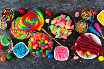 Wall Mural - Colorful sweet candy buffet table scene. Above view over a dark stone background.