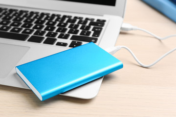 Charging modern laptop with power bank on wooden table, closeup