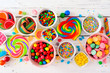 Colorful sweet candy buffet table scene. Top view over a white wood background.