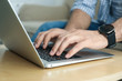 © New Africa - Man working on modern laptop at wooden table indoors, closeup