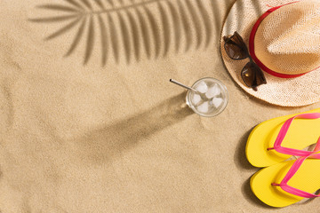 Wall Mural - Top view straw hat, sunglasses and glass of water with copy space. Traveler accessories on sand. Travel vacation concept. Summer background. Harsh light with shadows