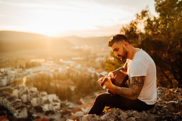 Young guitarist playing acoustic guitar and looking to sunset.Searching inspiration.Music creator.New artist.Musical talent.Handsome guitarist enjoying sunset and playing acoustic guitar.