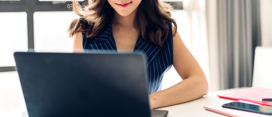 Beautiful confident asian businesswoman relaxing looking at technology of laptop computer while sitting on office desk.Young creative coworkers business people working and typing on keyboard at office