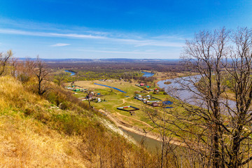 Top view of the bend of the river, two banks, bare branches against the blue sky on a spring day