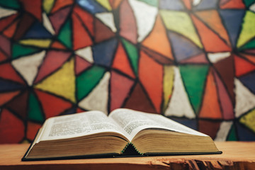 Close up open Holy Bible on a red wooden table. Beautiful Stained-glass windows background behind. Religion concept.