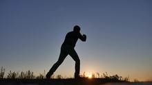 Man Is Training Doing An Imitation Boxing Shadow Fight Lifestyle. Martial Arts Concept. Silhouette Man On A Hill Nature Sunlight Engaged In Hand-to-hand Combat