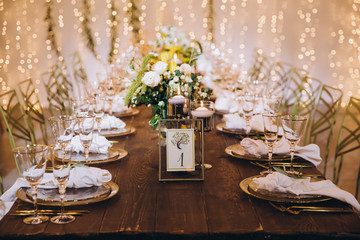 Wedding banquet. Table setting. Banquet tables are decorated with compositions of yellow flowers and lemons, on the tables are plates with napkins, glasses, candles and cutlery