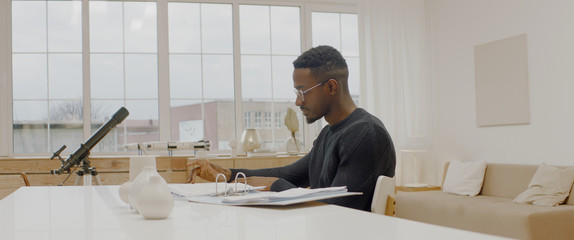 handsome african american male working from home, using laptop in living room, checking documents