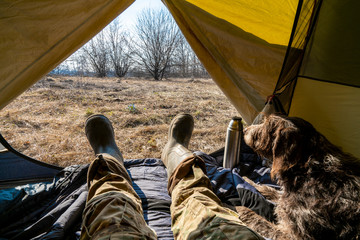view from a tourist tent, legs dressed in camouflage and hiking boots sticking out of the tent and n