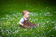 © Elena  - Charming boy among green grass and beautiful daisies on a summer day. A small child has fun in the fresh air. Baby explores the nature of