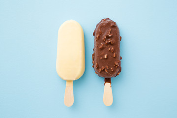 Two ice creams with dark and white chocolate glaze on pastel blue color table background. Closeup. Top down view.