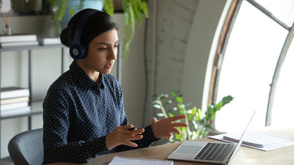 Canvas Print - Concentrated young indian businesswoman wearing wireless headset, holding educational video conference call with partners, discussing project details with client online, working remotely from home.