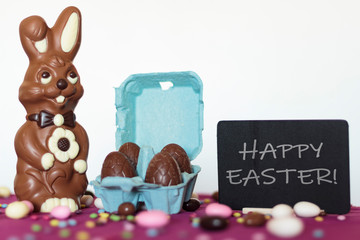 Wall Mural - Chocolate bunny, egg carton with chocolate eggs and blackboard with the text Happy Easter