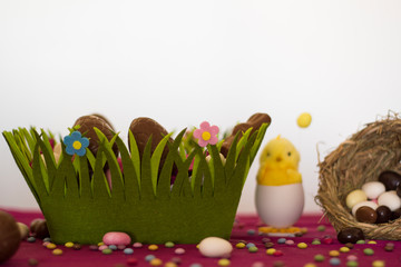 Canvas Print - Easter basket with chocolate eggs, decorative chick, bird nest with easter almonds and other sweets on table