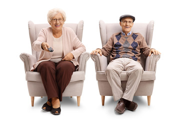 Poster - Senior couple sitting in an armchairs and holding a tv remote control