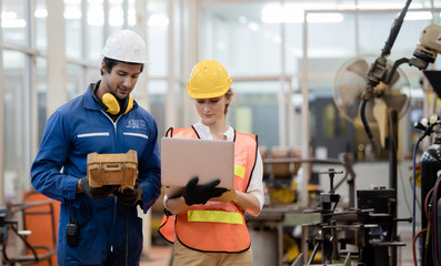 Engineer and worker control and check robot working in factory. The worker is controlling the robot to work in the factory.