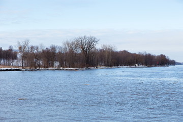 Wall Mural - Pretty St. Lawrence River cove, farm and scattering of houses seen through bare branches during an early spring morning, Lotbinière, Quebec, Canada