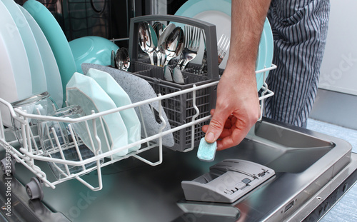 Loading the tablet into the dishwasher. A man puts the tablet in the dishwasher to wash dirty dishes.