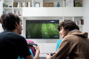 two boys sitting at home playing video games on game console