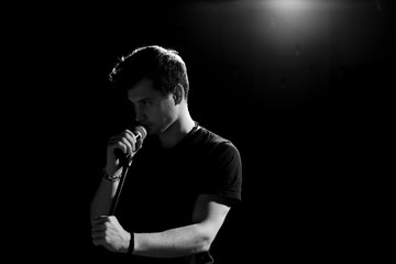 Young handsome guy emotionally sings and speaks into the microphone. Black and white photography