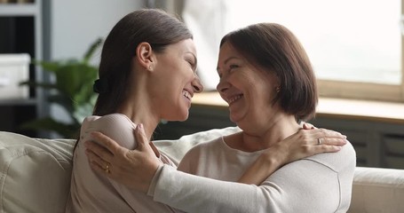 Wall Mural - Affectionate young woman cuddling bonding middle aged mature mother, enjoying sweete tender moment together at home. Head shot happy loving two female generations family communicating indoors.