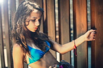portrait of a beautiful young girl in blue swimsuit leaned against a wooden fence.