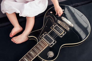 Little baby’s hand on a black electric guitar.