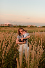 A mother walks in the field with her little daughter in her arms.