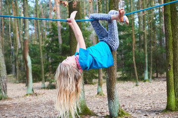 Wall Mural - Young child girl hanging on rope upside down on playground in park