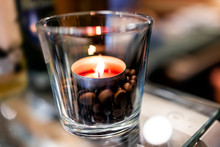 Macro Closeup Of Small Tea Red Candle Light On Glass Table In Cup Cafe Restaurant Romantic Atmosphere Blurry Background And Roasted Coffee Beans