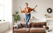 © JenkoAtaman - Cheerful woman listening to music and dancing on soft couch at home in day off.